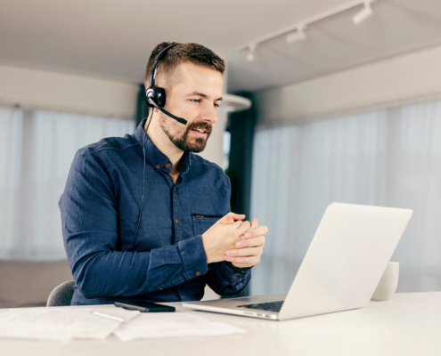 Side view of young man with headset working on laptop and talking