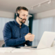 Side view of young man with headset working on laptop and talking